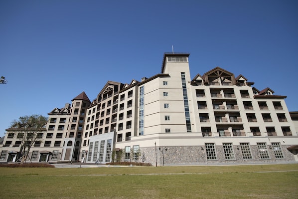 Een hotel met meerdere verdiepingen, een centraal torentje, balkons en een verzorgd gazon.