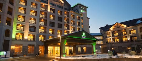 A multi-story hotel with a central entrance, balconies on each floor, and a snow-covered ground.