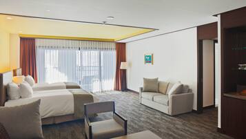 A hotel room with two beds, a sofa, a chair, a small table, and a kitchenette.