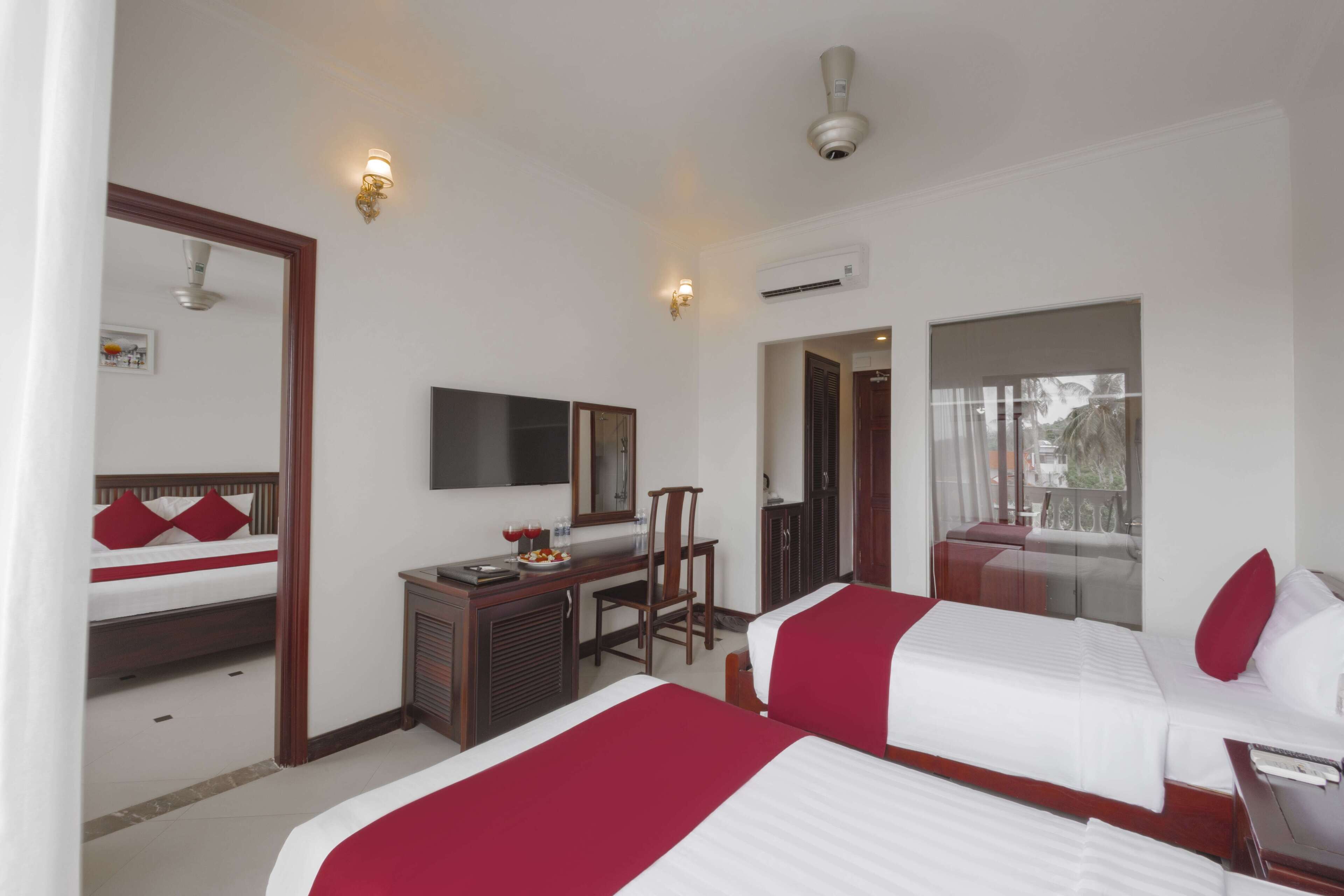 A hotel room with two beds, a desk with a chair, a mirror, and an air conditioning unit.