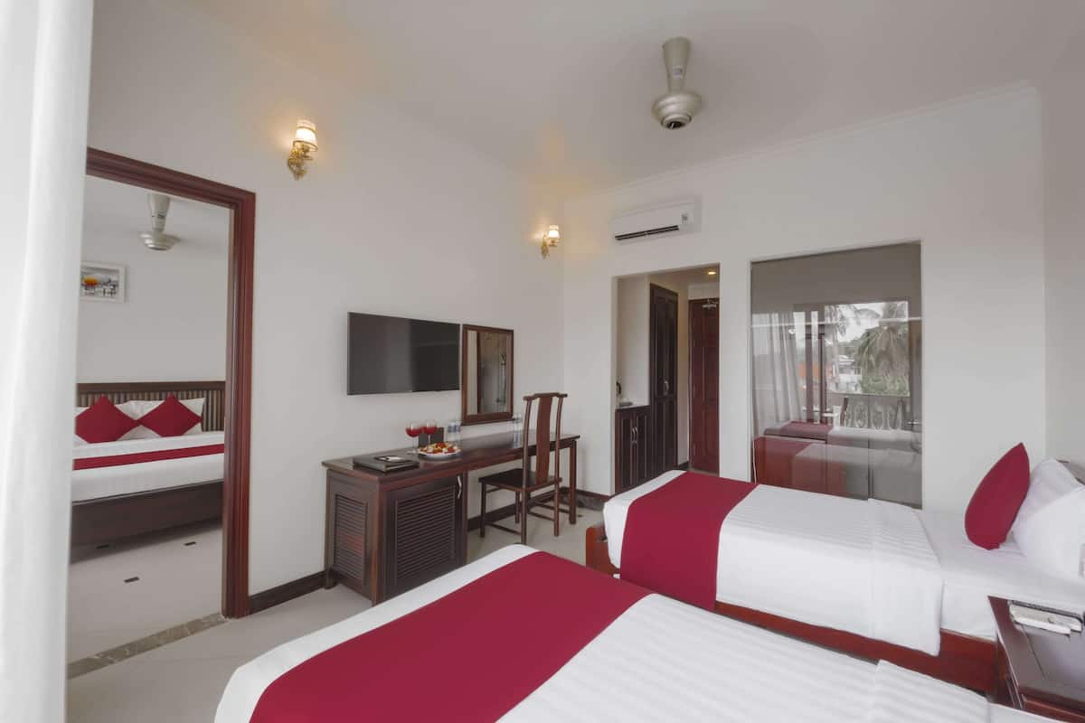 A hotel room with two beds, a desk with a chair, a mirror, and an air conditioning unit.