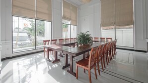 Un salón de conferencias con una larga mesa, sillas, ventanas amplias con persianas y una lámpara colgante.