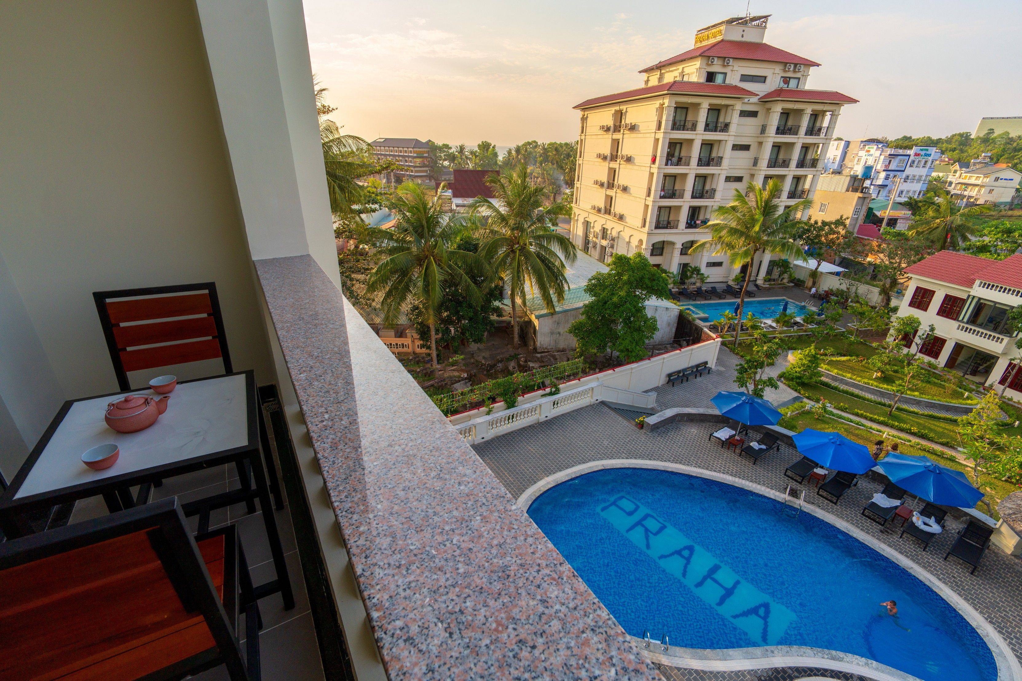 A pool area with a sign reading "PRAHA" and a view of surrounding buildings and palm trees.