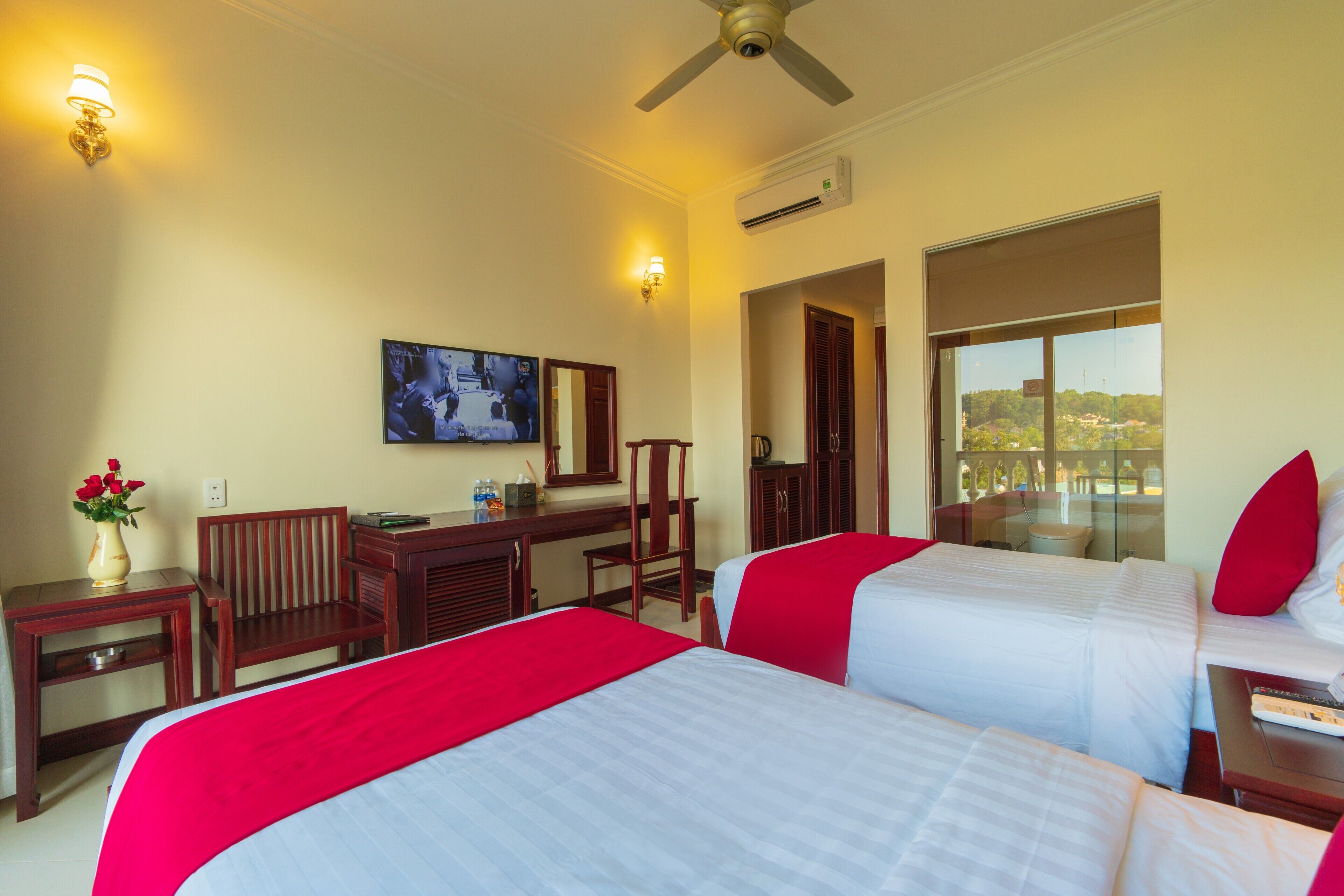 A hotel room with two beds, a desk, a chair, a TV, and a large window with a view.
