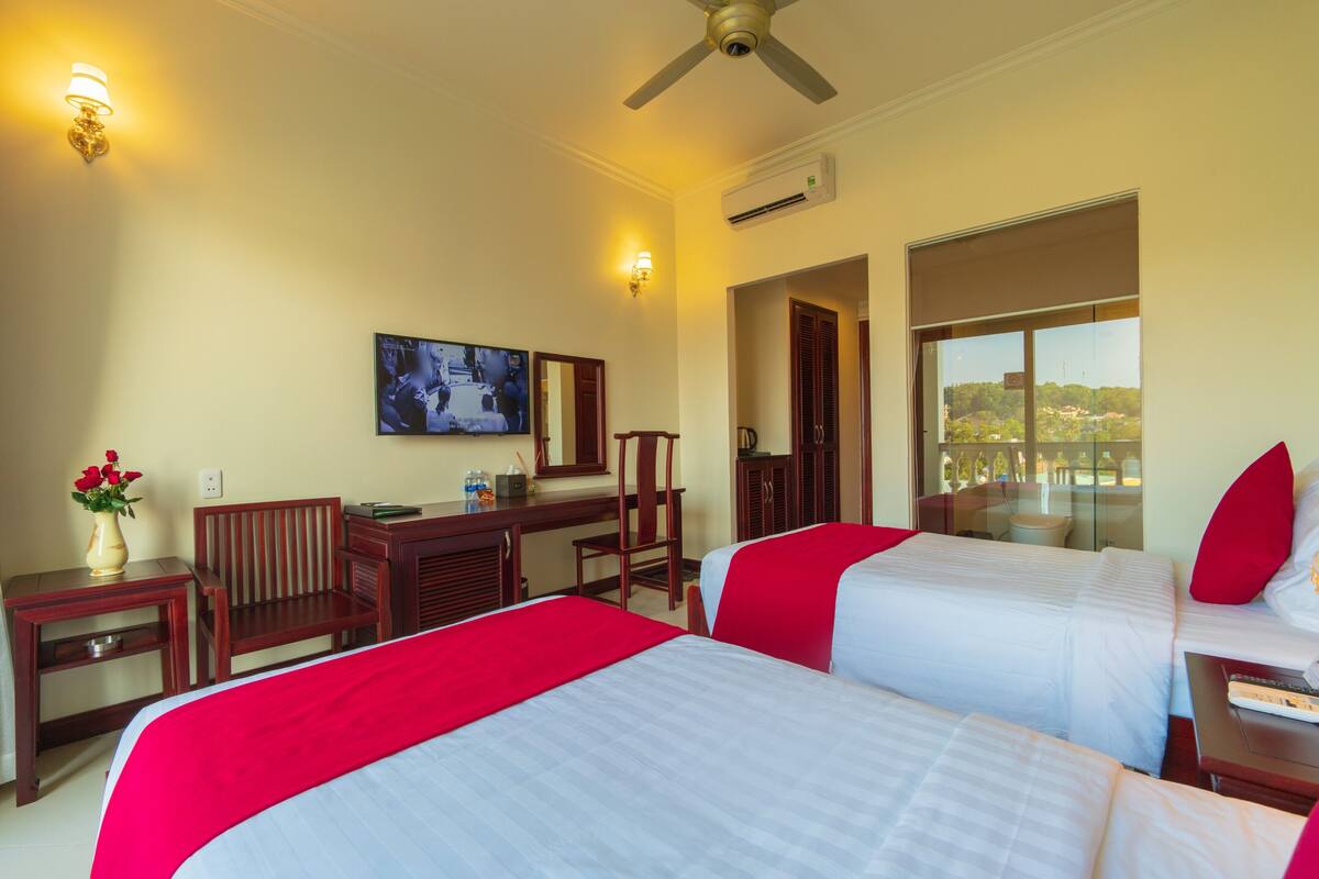 A hotel room with two beds, a desk, a chair, a TV, and a window with a view.