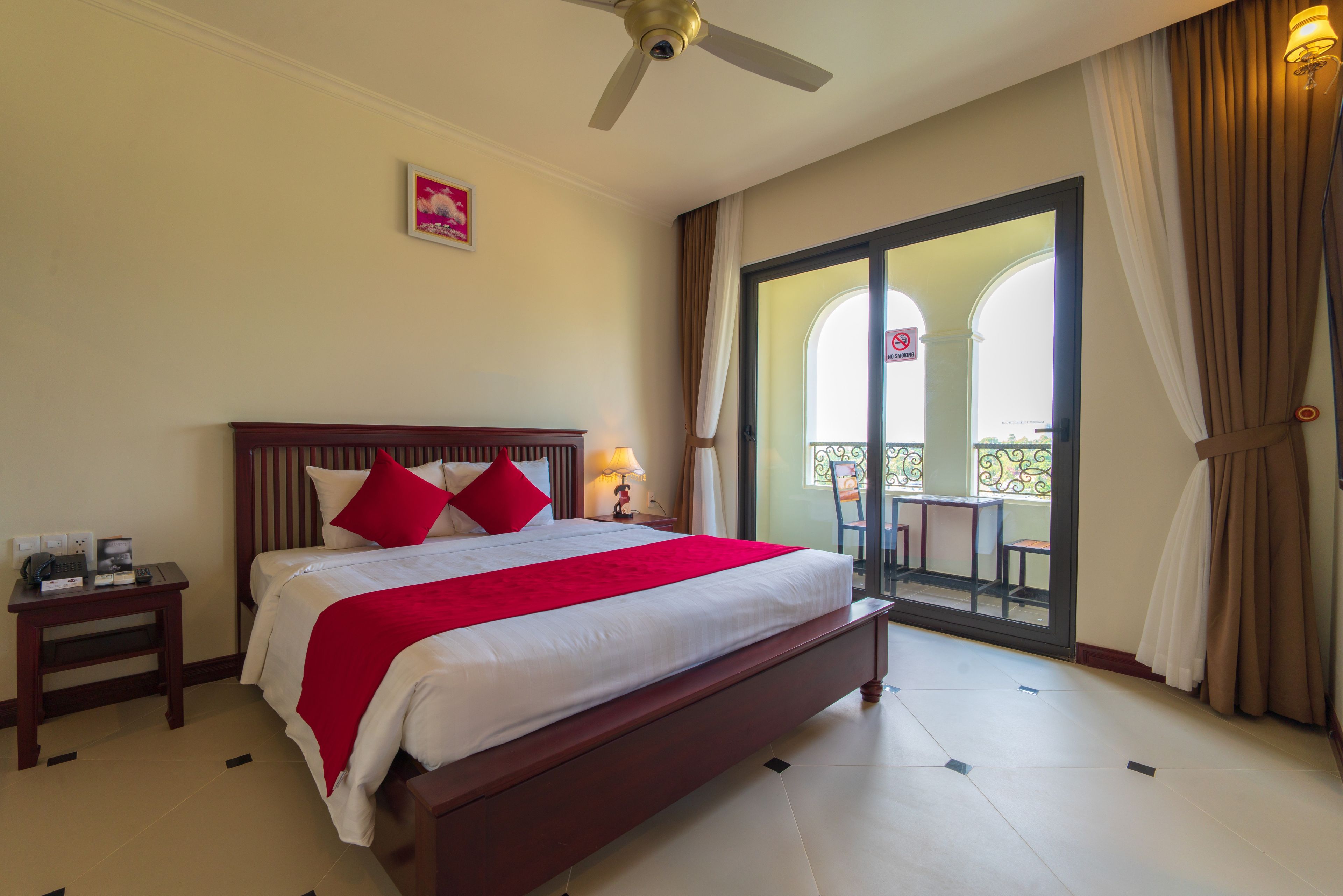 A hotel room with a large bed, a nightstand, a ceiling fan, and a view of the outdoor balcony.