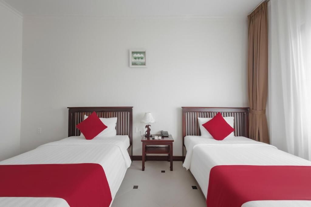 A hotel room with two beds, a nightstand, a lamp, and a framed picture on the wall.