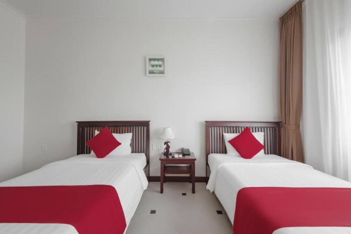 A hotel room with two single beds, a nightstand, a lamp, and a small framed picture on the wall.