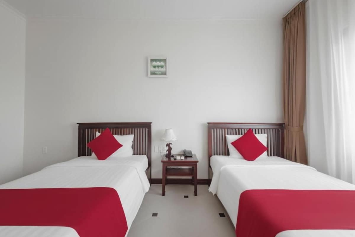 Habitación de hotel con dos camas individuales, una mesita de noche, una lámpara y un pequeño cuadro en la pared.