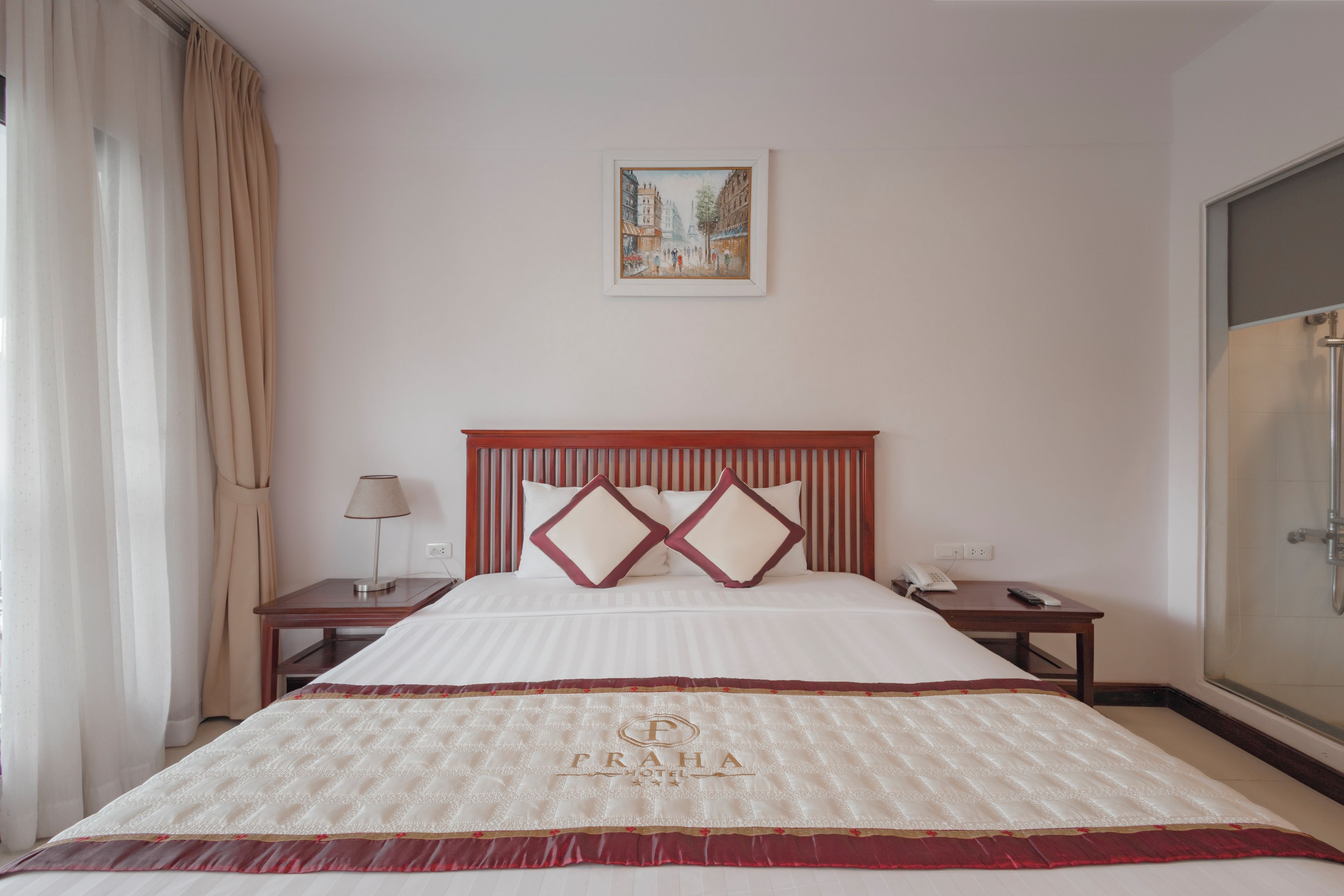 A hotel room with a large bed, a nightstand, a lamp, a framed picture on the wall, and a shower area.