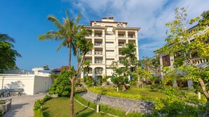 Un hotel de varios pisos con un jardín ajardinado, palmeras y un camino pavimentado.