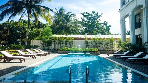 Una piscina con sillones de descanso, palmeras y un edificio con balcones.