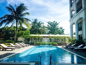 A swimming pool with lounge chairs, palm trees, and a building with balconies.