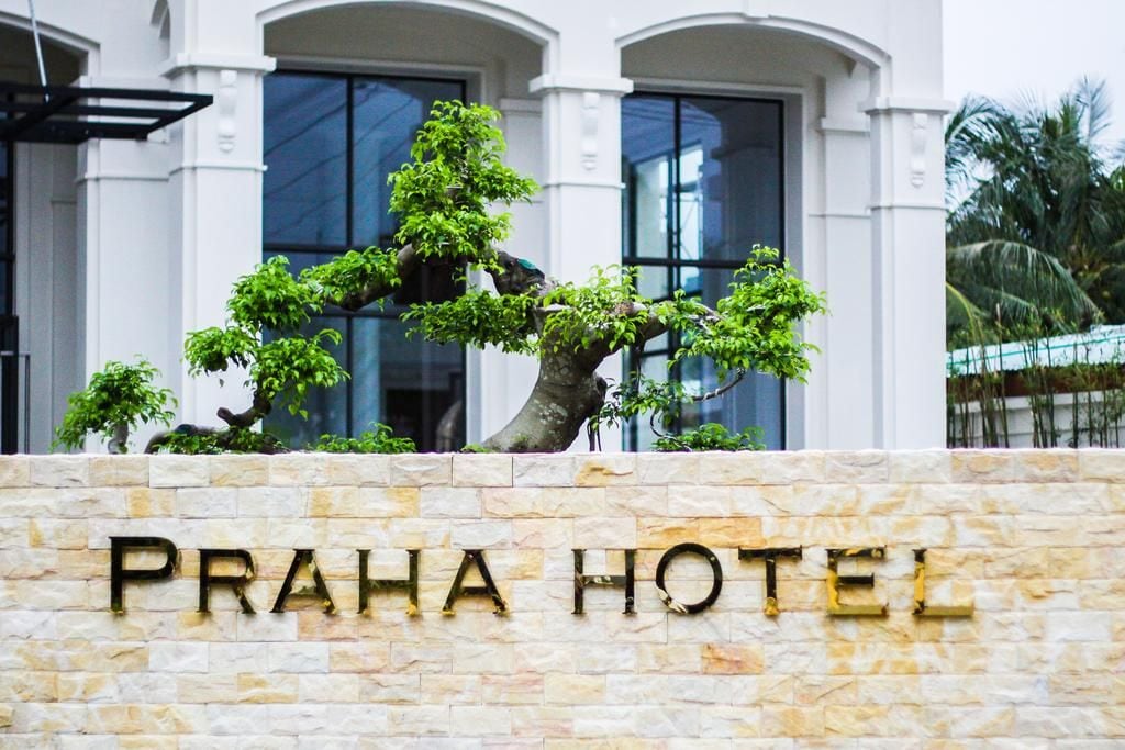 A stone wall with the text 'PRAHA HOTEL' and a bonsai tree in front.