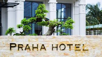 A stone wall with the text 'PRAHA HOTEL' and a bonsai tree in front.