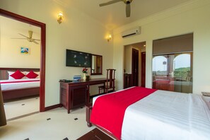 Habitación de hotel con cama, escritorio, televisor y balcón con vistas.