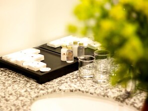 Uma bancada com uma bandeja contendo diversos itens, incluindo garrafas e copos, provavelmente para um minibar ou área de bar.