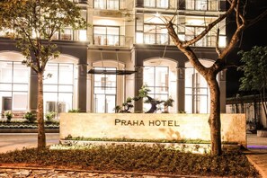 Ein Hotel Eingang mit einem Schild, auf dem 'PRAHA HOTEL' steht, umgeben von Bäumen und einer gut beleuchteten Fassade.