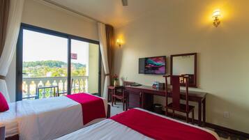 A hotel room with two beds, a desk, a chair, a TV, and a balcony with a view.