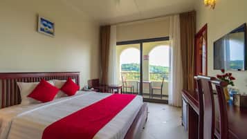 A hotel room with a large bed, a balcony with a view, a TV, and a desk with a chair.