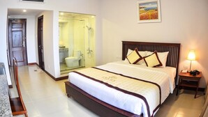 Habitación de hotel con una cama grande, una mesita de noche con lámpara, un baño con cabina de ducha de cristal y un cuadro en la pared.