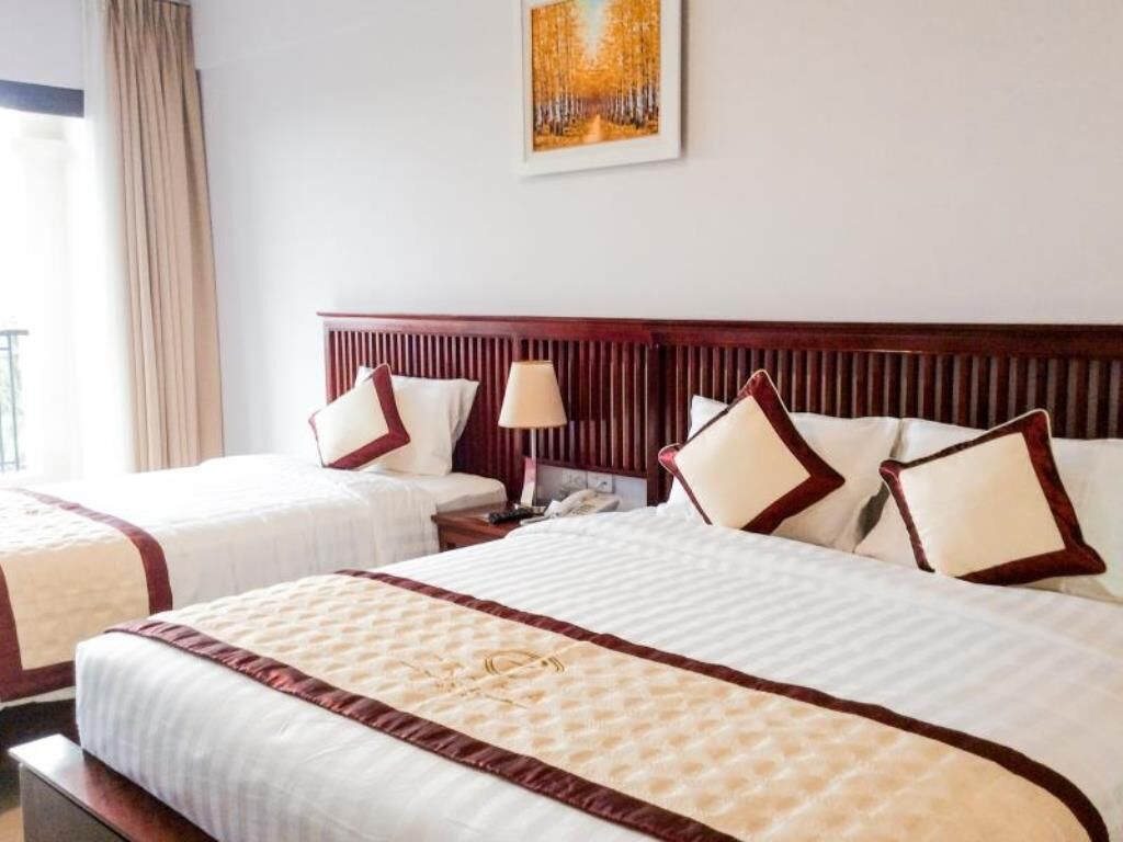 A hotel room with two beds, a wooden headboard, a nightstand, a lamp, and a painting on the wall.