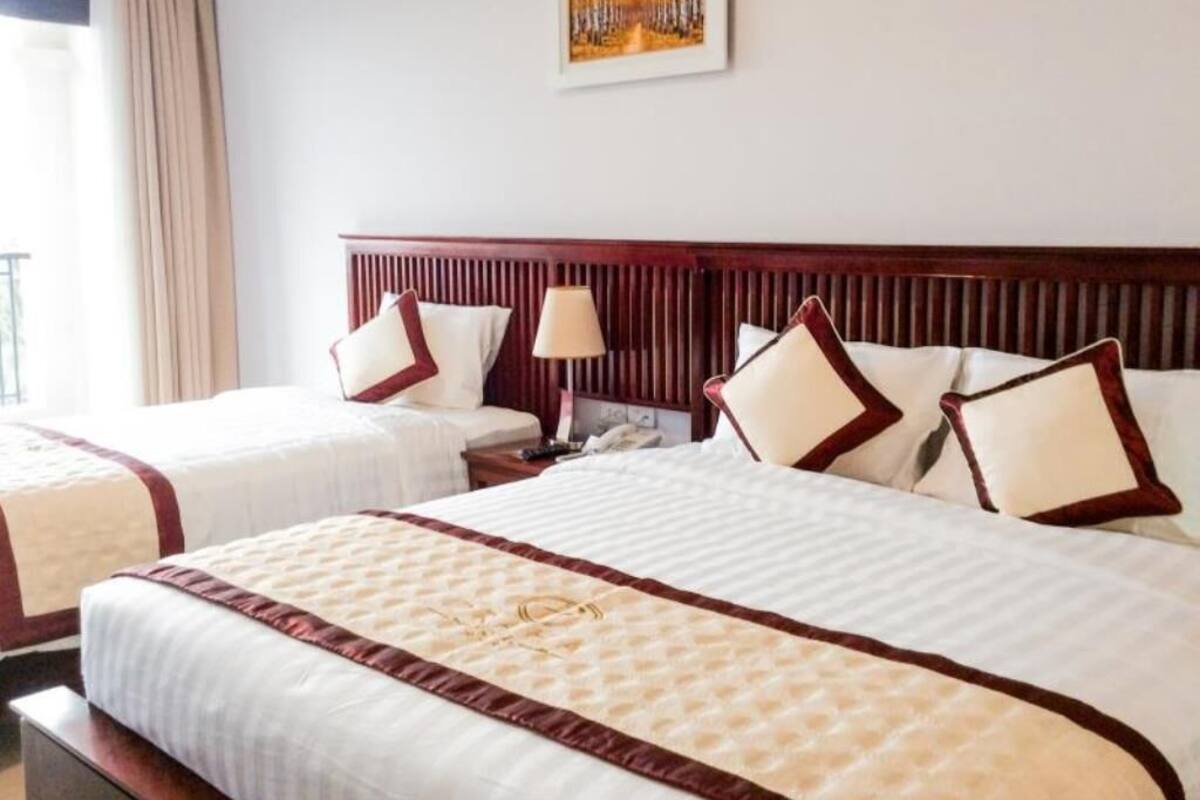 A hotel room with two beds, a wooden headboard, a nightstand, and a painting on the wall.