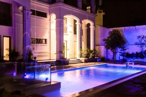 A nighttime view of a building with a swimming pool, illuminated by purple lighting, and a fountain. - Praha Hotel Phu Quoc (Phu Quoc)