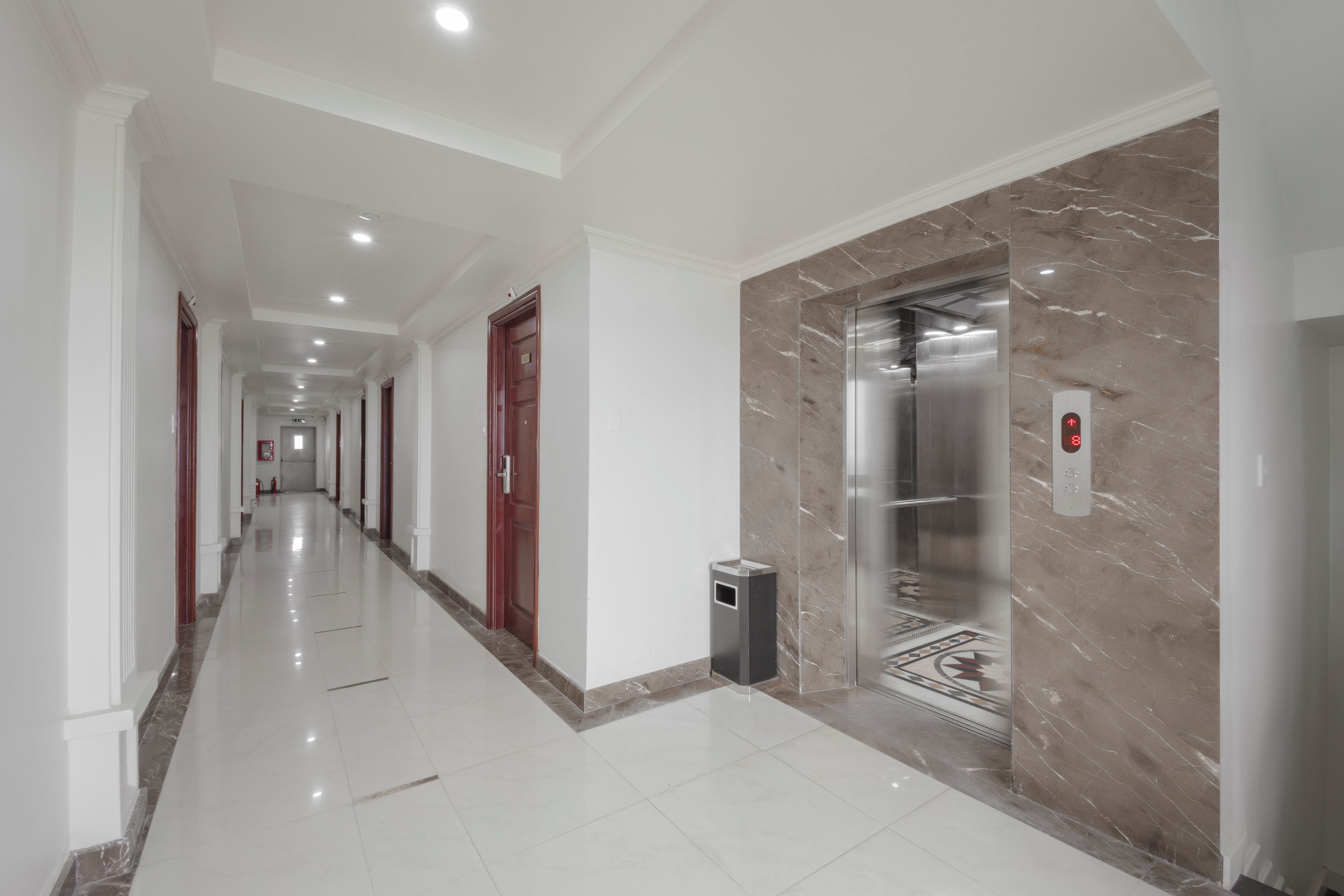 A long, well-lit hallway with a marble wall and an elevator.