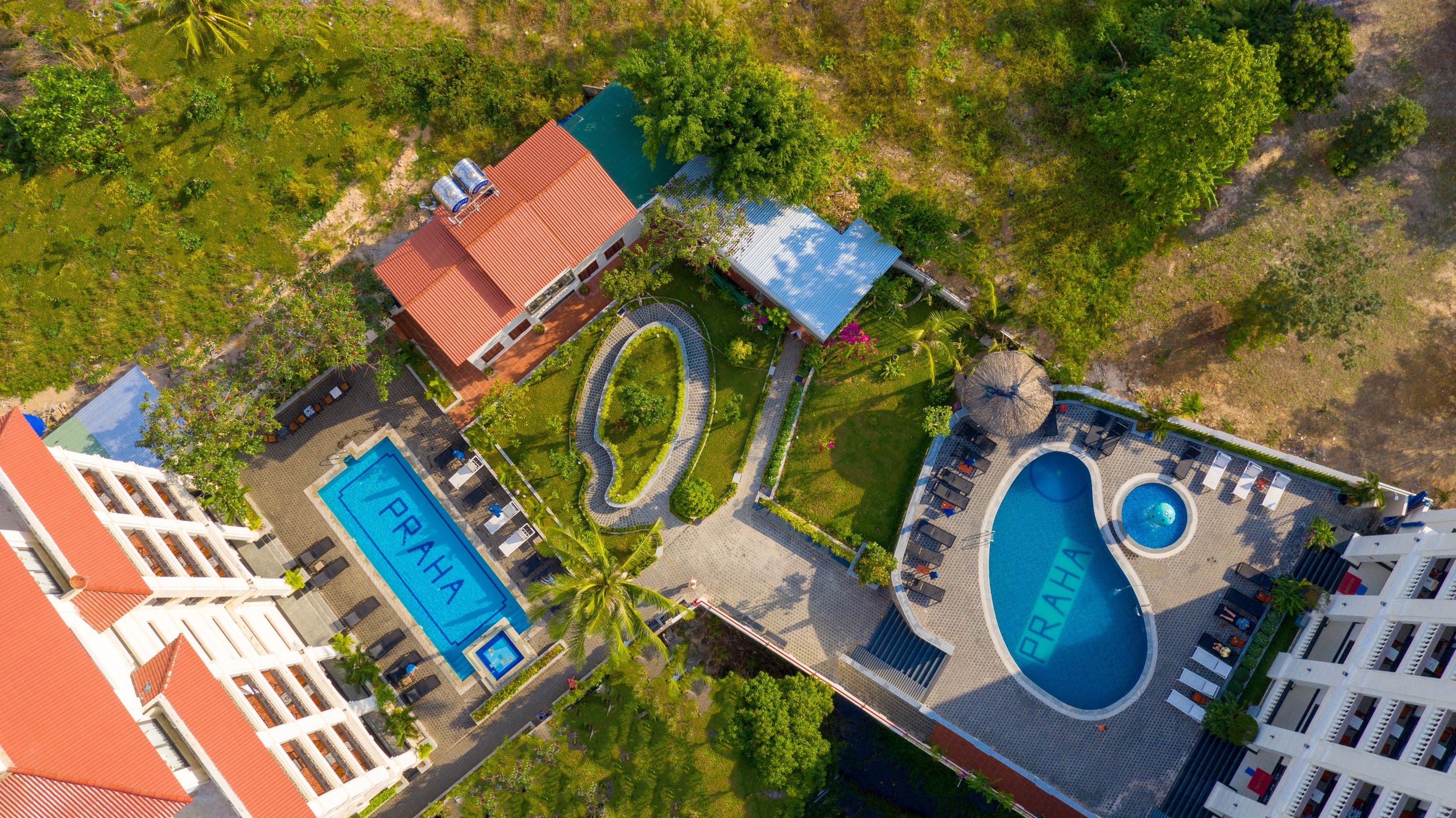 An aerial view of a resort with a large central pool, smaller pools, and a circular water feature.