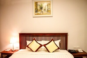Quarto de hotel com cama, mesa de cabeceira com abajur, telefone e um quadro na parede.