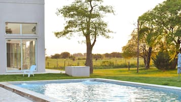 Ein modernes Haus mit Swimmingpool, Rasen und Baum.