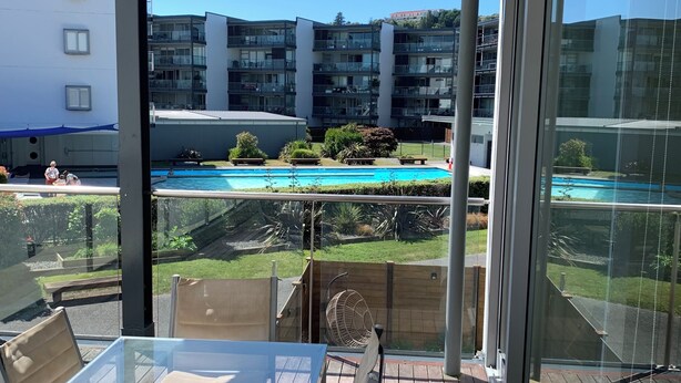 An outdoor balcony with a glass table and chairs, overlooking a swimming pool and residential buildings. - Location, location, location - as good as it gets in Napier (Napier)