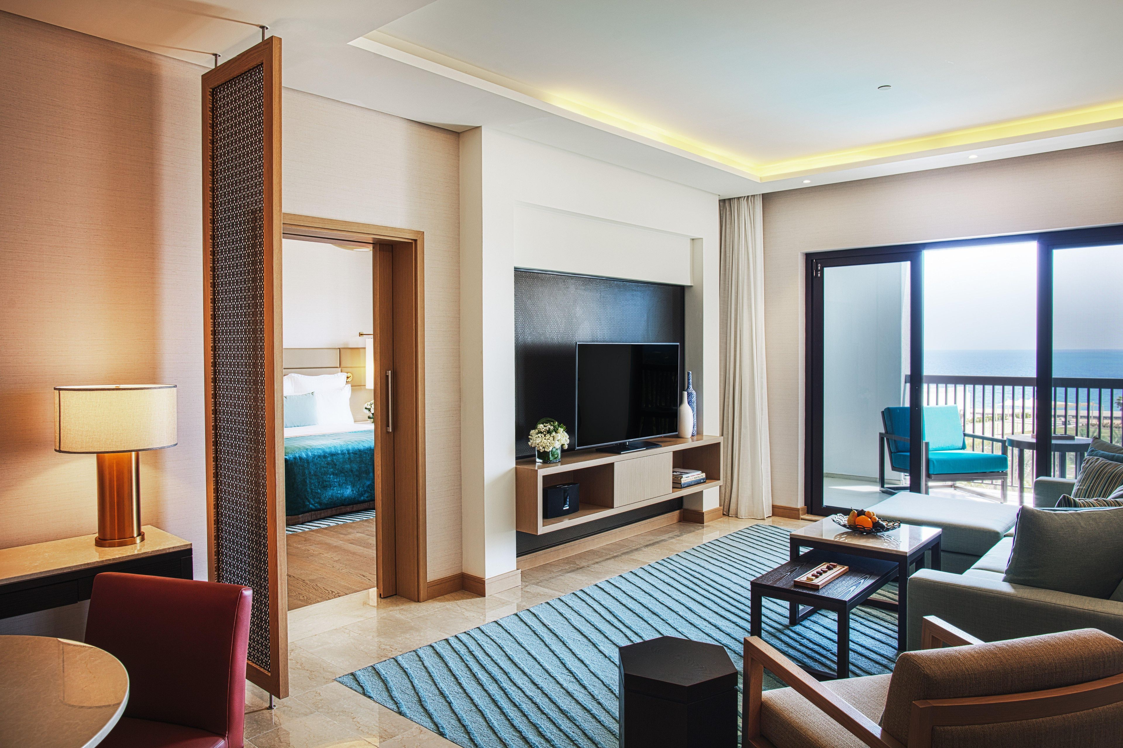 A hotel room with a bed, a TV, a seating area with a table and chairs, a balcony with a view, and a decorative screen.