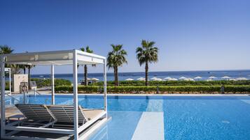 A clear blue pool with lounge chairs, palm trees, and a view of the ocean.