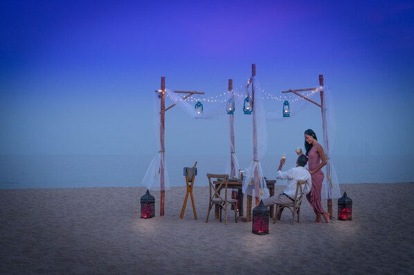 Un décor de plage avec une structure en bois, des lanternes et une table entourée de chaises.