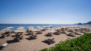 A beach with rows of sun loungers and umbrellas, a clear sky, and calm sea.
