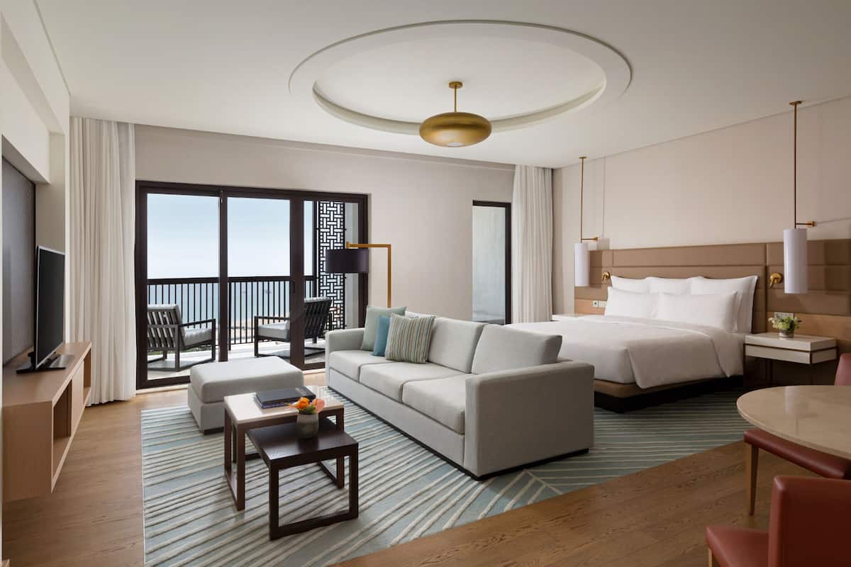 A hotel room with a bed, sofa, TV, and a balcony with a view.