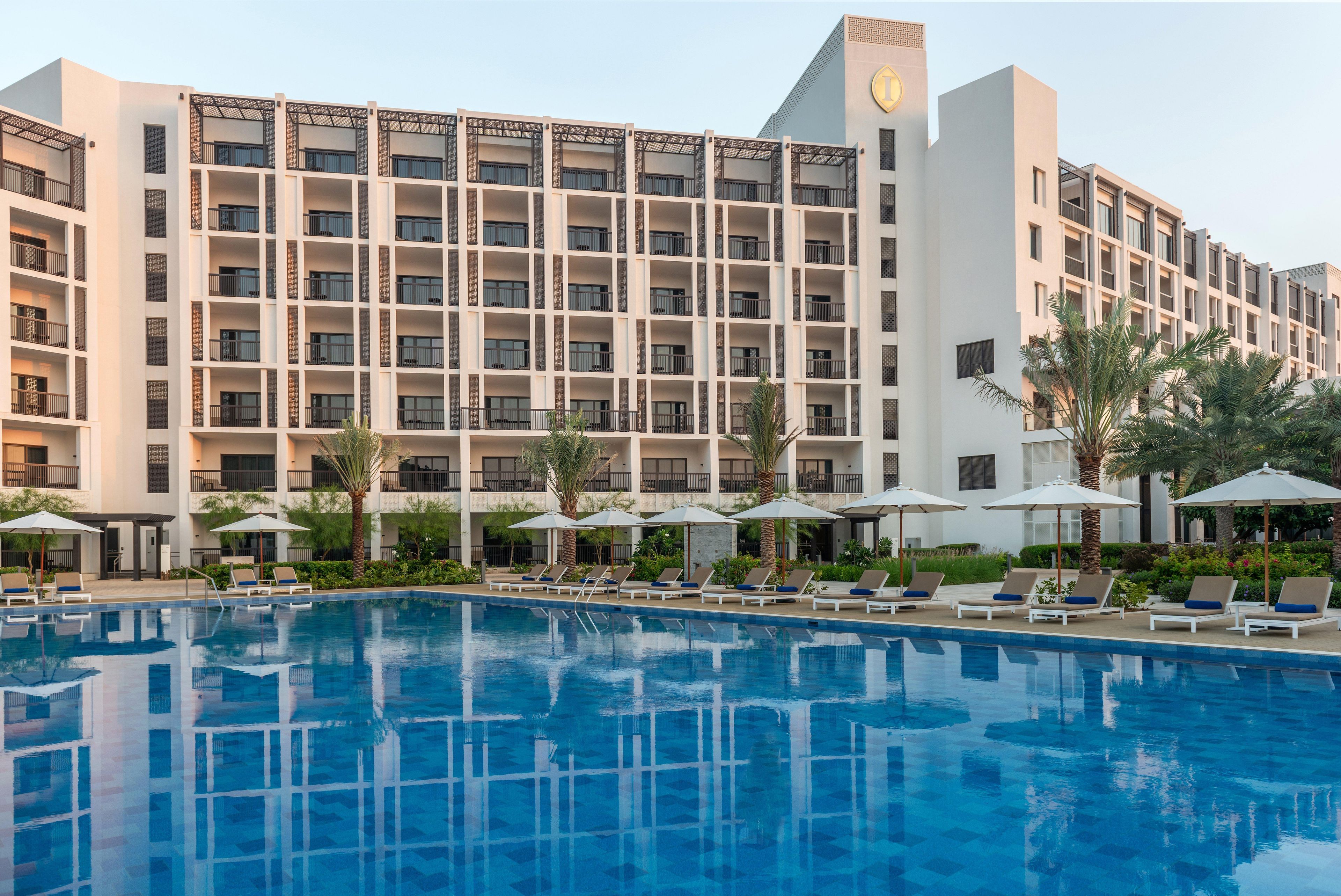 A hotel with a swimming pool, sun loungers, and palm trees.