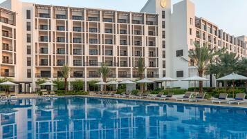 A hotel with a swimming pool, sun loungers, and palm trees.