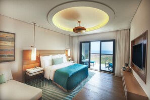 A hotel room with a large bed, a desk, a chair, a TV, and a balcony with a view.
