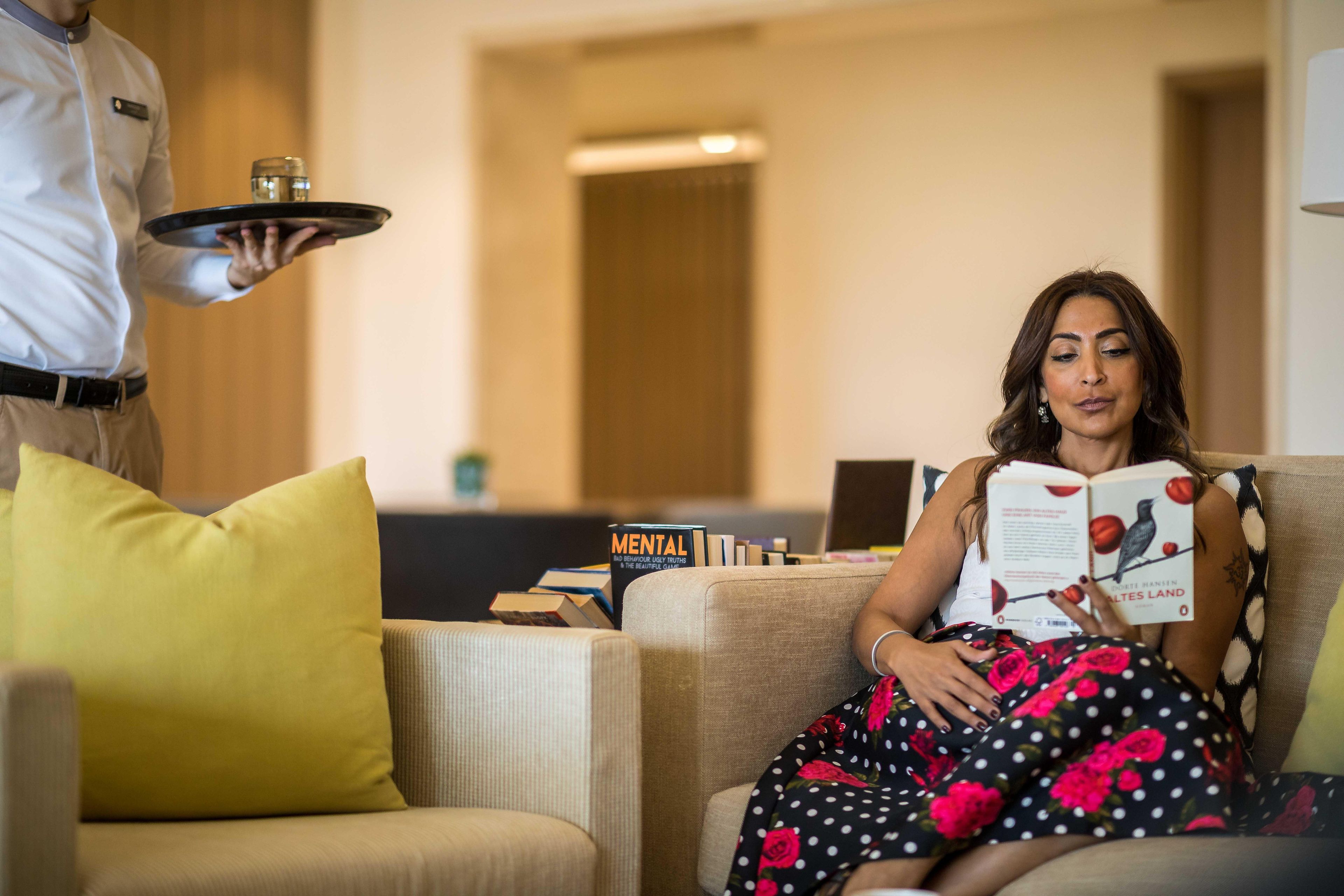 A person seated on a sofa with a tray of items held by another person.