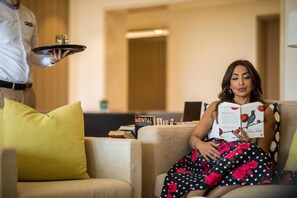 A person seated on a sofa with a tray of items held by another person.