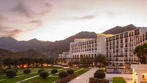 Un hotel con varios pisos, un jardín cuidado con setos podados y un área de piscina.