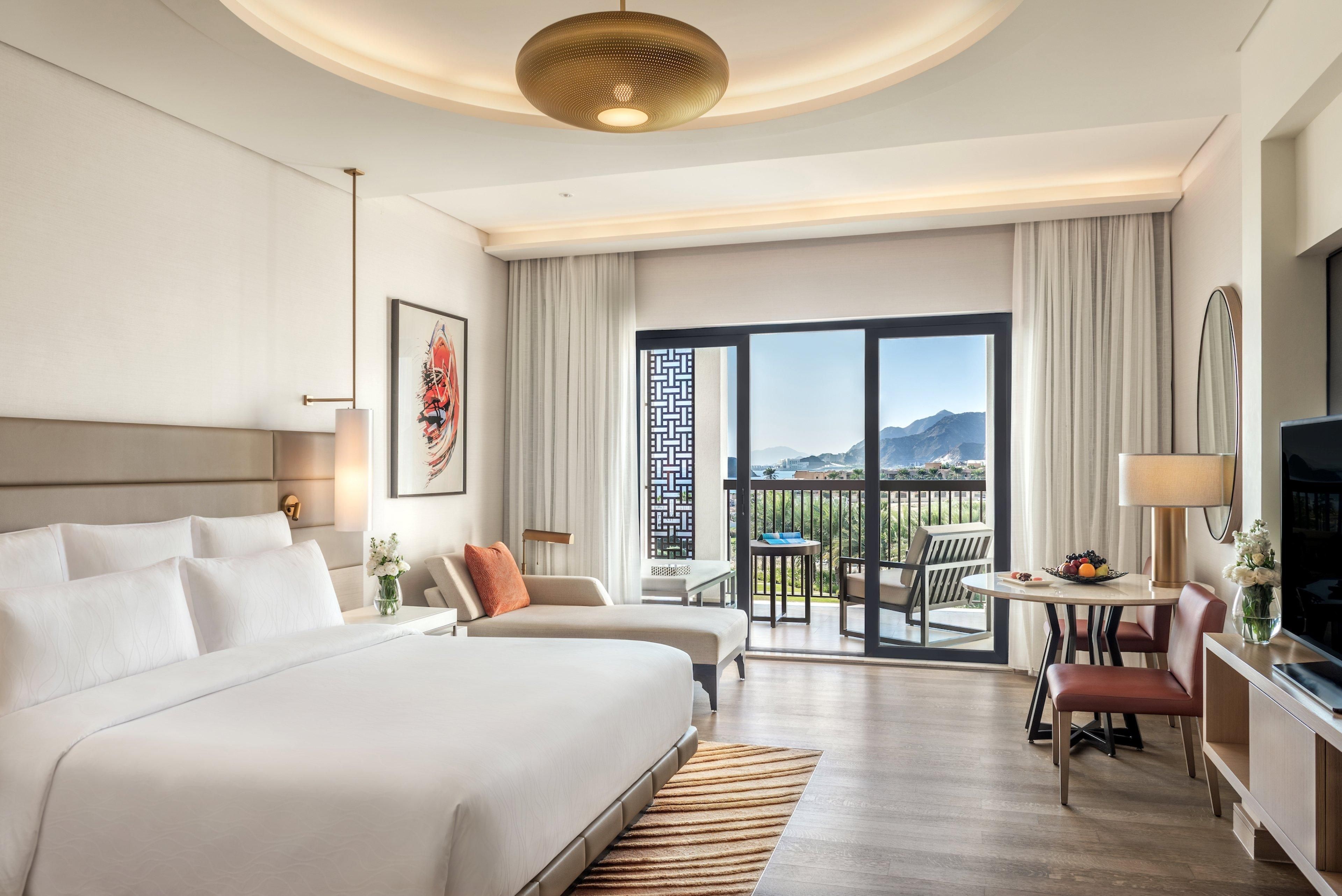 Ein Hotelzimmer mit einem großen Bett, einem Schreibtisch mit Stuhl, einem Fernseher und einem Balkon mit Aussicht.