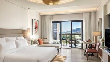 Ein Hotelzimmer mit einem großen Bett, einem Schreibtisch mit Stuhl, einem Fernseher und einem Balkon mit Aussicht.