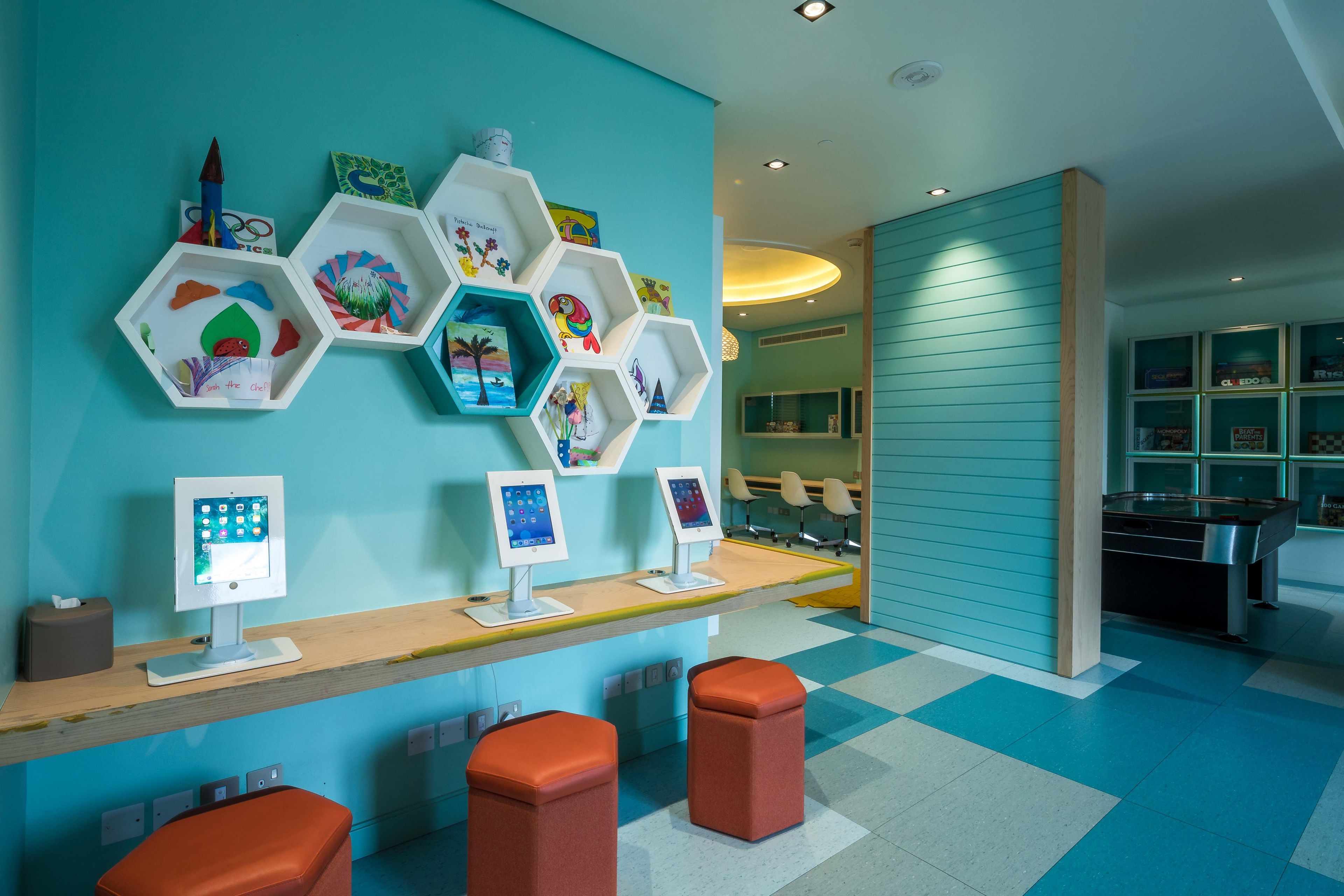 Un espace d’accueil avec un mur de couleur turquoise, des étagères hexagonales, deux écrans d’ordinateur et des tabourets orange.