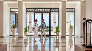 En moderne hotellobby med spejlblankt gulv, store vinduer og potteplanter.