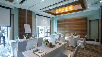 A conference room with white tables, chairs, a projector screen, and a wooden panel wall.