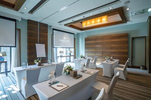 A conference room with white tables, chairs, a projector screen, and a wooden panel wall. - Intercontinental Fujairah Resort (FUJAIRAH)